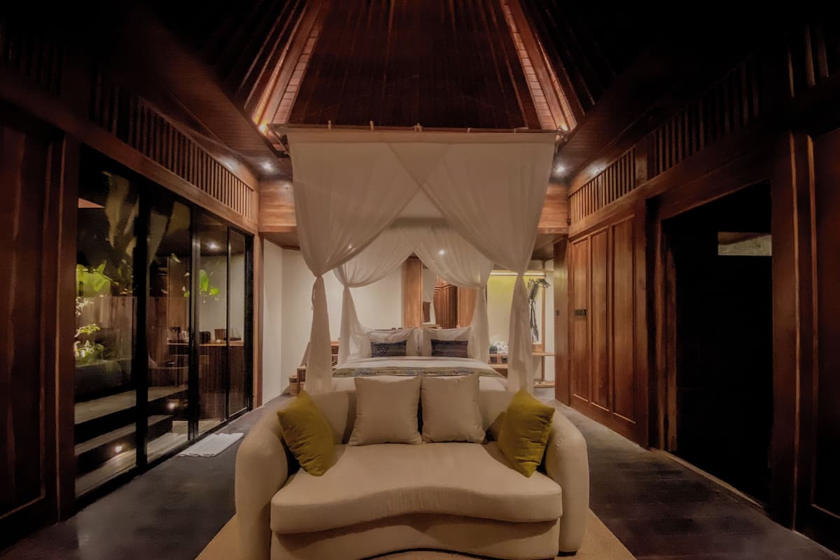 A bedroom with a canopy bed, a sofa, and a large window.