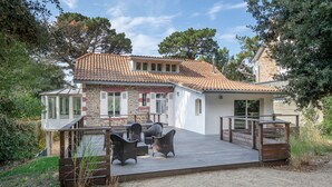 Une maison avec un toit en tuiles, une terrasse en bois et du mobilier d’extérieur.