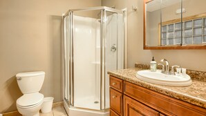 Une salle de bain dotée d’une douche à parois de verre, de toilettes blanches, d’un lavabo avec un plan de travail en granit et de meubles en bois.