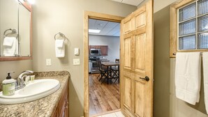 Une salle de bain équipée d’un lavabo, d’un miroir et d’une porte en bois donnant sur un coin repas avec une table et des chaises.
