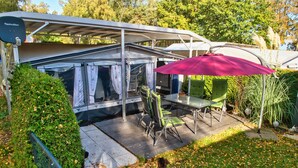 En overdækket terrasse med et bord, stole, grill og et markise.