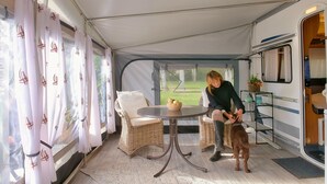 Et overdækket område med fletningsmøbler, et bord med en skål frugt og en hund.