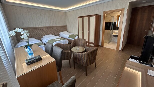 Une chambre d’hôtel comprenant un lit, deux tables de chevet, un bureau avec une chaise, une petite table ronde avec deux chaises, une armoire et une salle de bain visible à travers une porte ouverte.