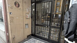 Une entrée d’immeuble avec un mur recouvert de carreaux, un portail en métal et un sol carrelé menant à une porte.