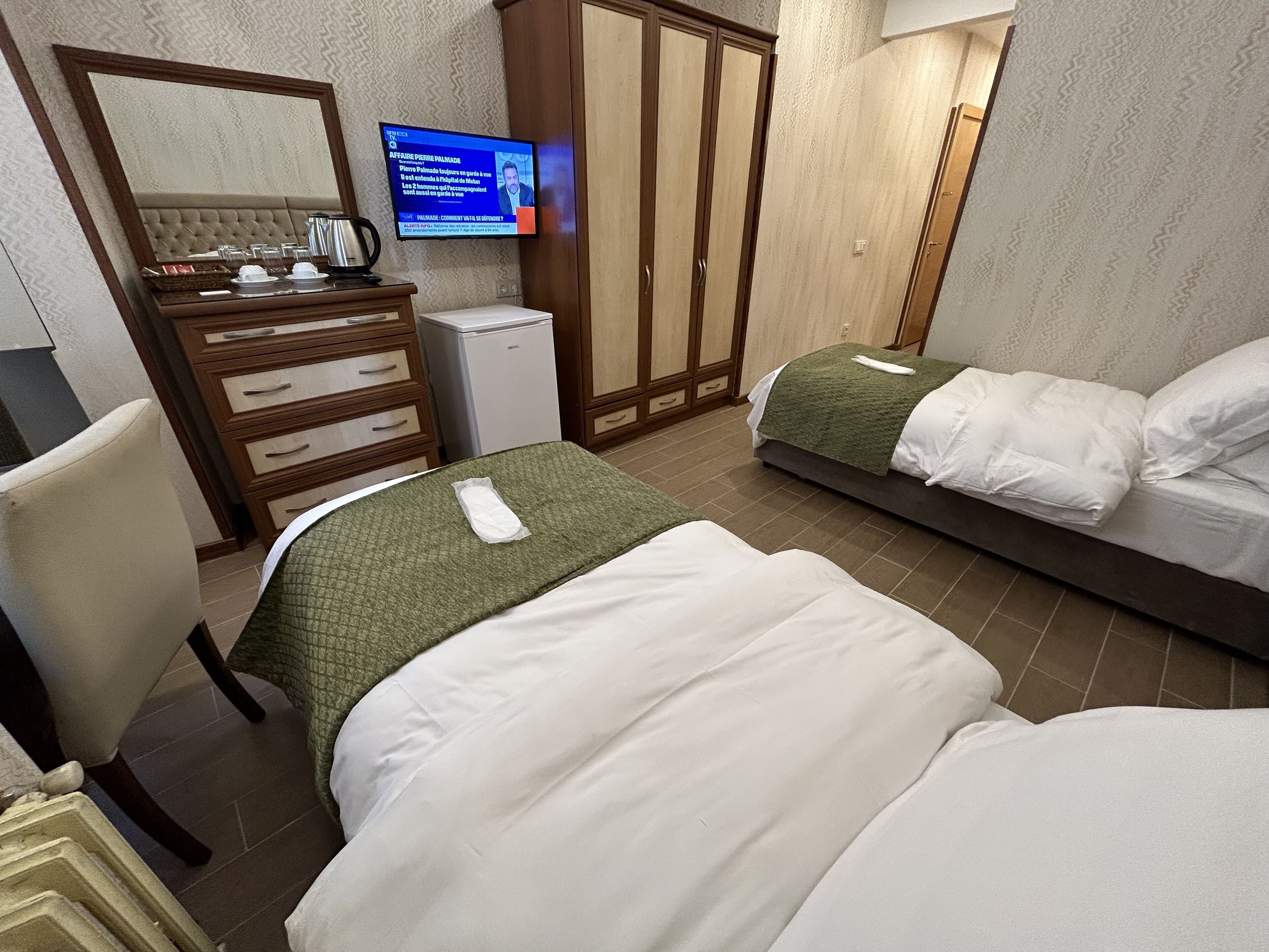 Een hotelkamer met twee bedden, een televisie, een kledingkast en een bureau met een waterkoker.