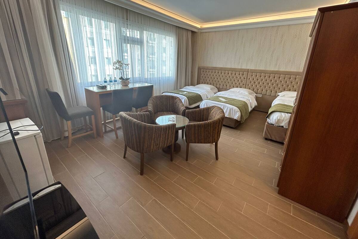 A hotel room with two beds, a desk, a chair, a small table, and a potted plant.
