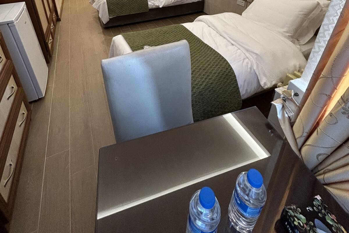 A hotel room with two beds, a desk, and a chair. There are two bottles of water on the desk.