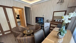 Un salon avec un téléviseur, un canapé et une table basse. On y trouve également un meuble en bois et un petit réfrigérateur.