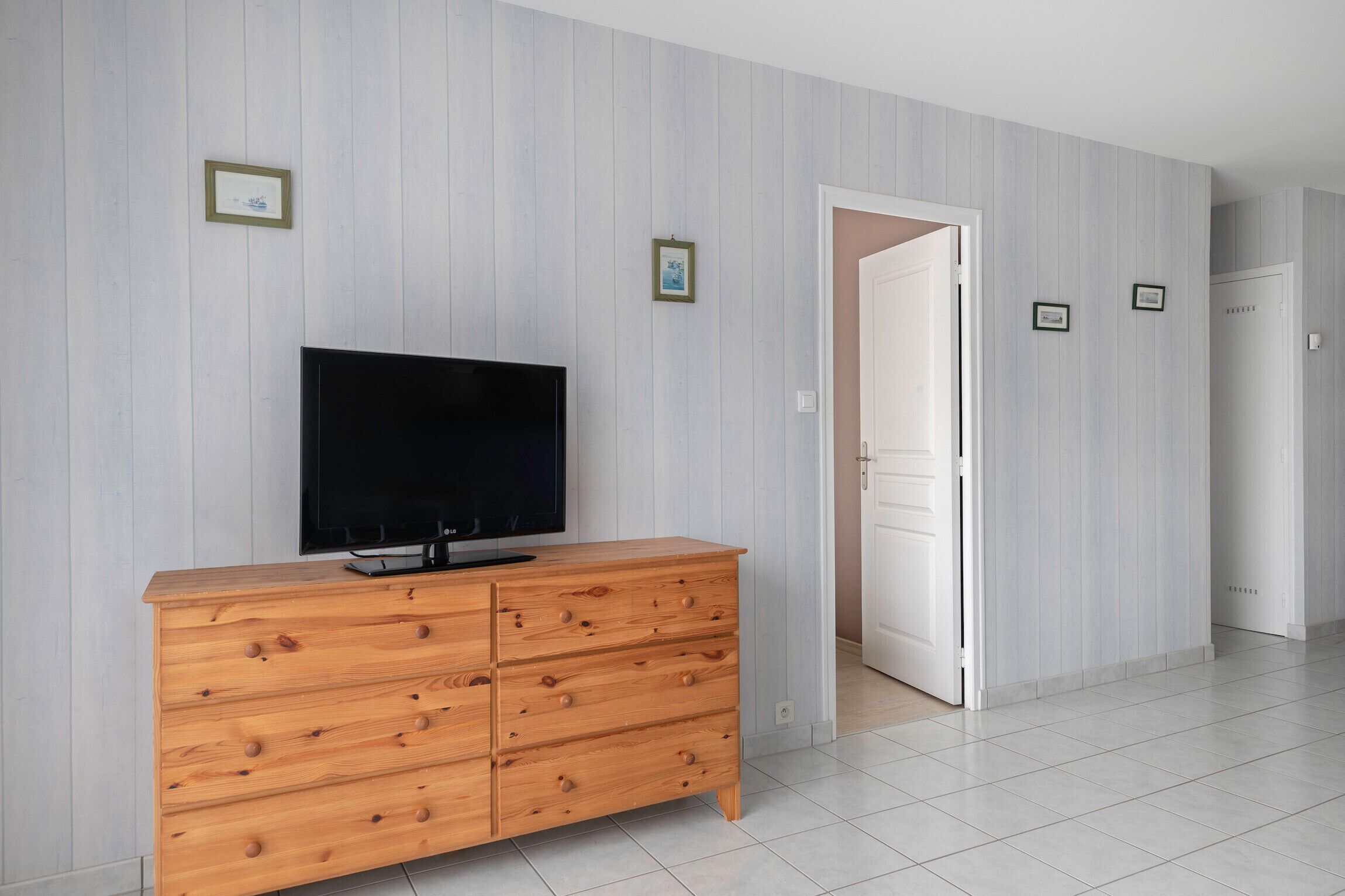 A room with a wooden dresser, a flat-screen TV, and a door leading to another room.