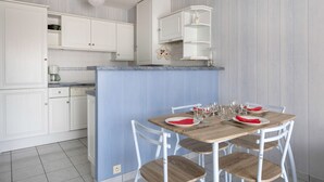 Una cocina compacta con armarios blancos, una isla azul y una mesa de comedor lista para cuatro comensales.