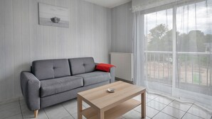Una sala de estar con un sofá gris, una mesa de centro de madera y un ventanal con cortinas ligeras.