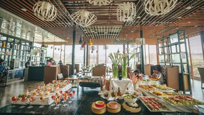 Ein reichhaltiges Buffet mit verschiedenen Speisen und Getränken, eine Bar mit Bedienung und ein modernes Interieur mit Holzbalken und hängenden Leuchten.