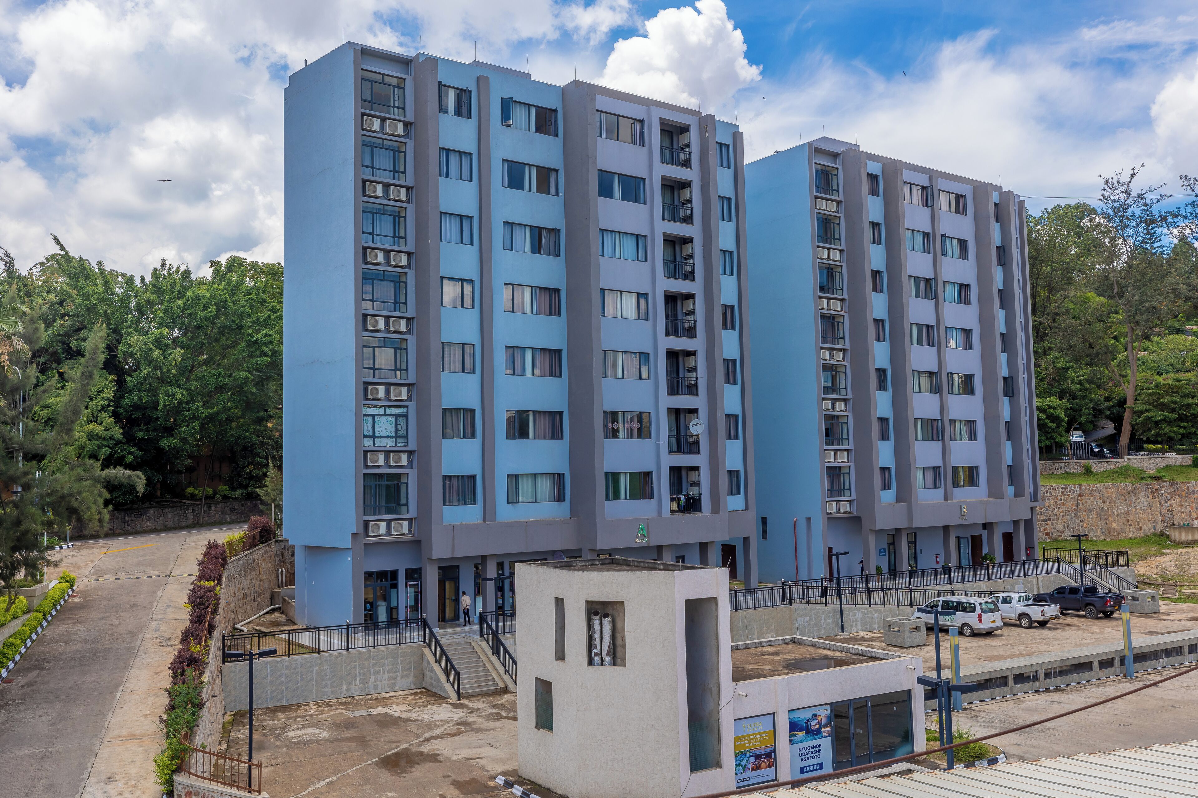 A multi-story residential building with balconies, a parking area, and a small garden area.