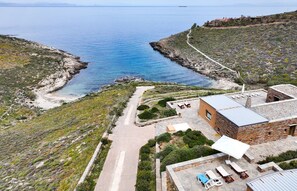 An aerial view of a coastal property with a stone building, a paved path, and a small patio area with outdoor furniture.