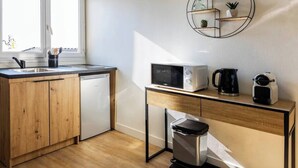 Una cocina compacta con armarios de madera, lavavajillas, microondas, cafetera y cubo de basura.