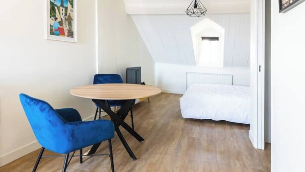 Una habitación con una cama, una mesa redonda y dos sillas azules.