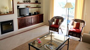 A living room with a fireplace, a television, wicker chairs, and a glass coffee table. - Presley Pink Apartment, Quinta do Lago, Algarve (Algarve)