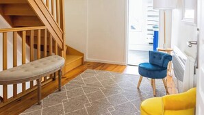 Eine Treppe mit gepolstertem Sitzbrett, einem blauen Stuhl und einem gelben Hocker in einem hell erleuchteten, mit einem gemusterten Teppich ausgelegten Flur.