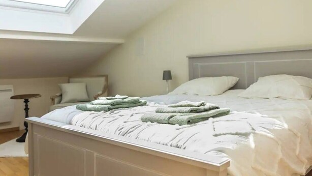 Ein Schlafzimmer mit schrägem Dach, einem Bett mit weißer Bettwäsche und einem Oberlicht.