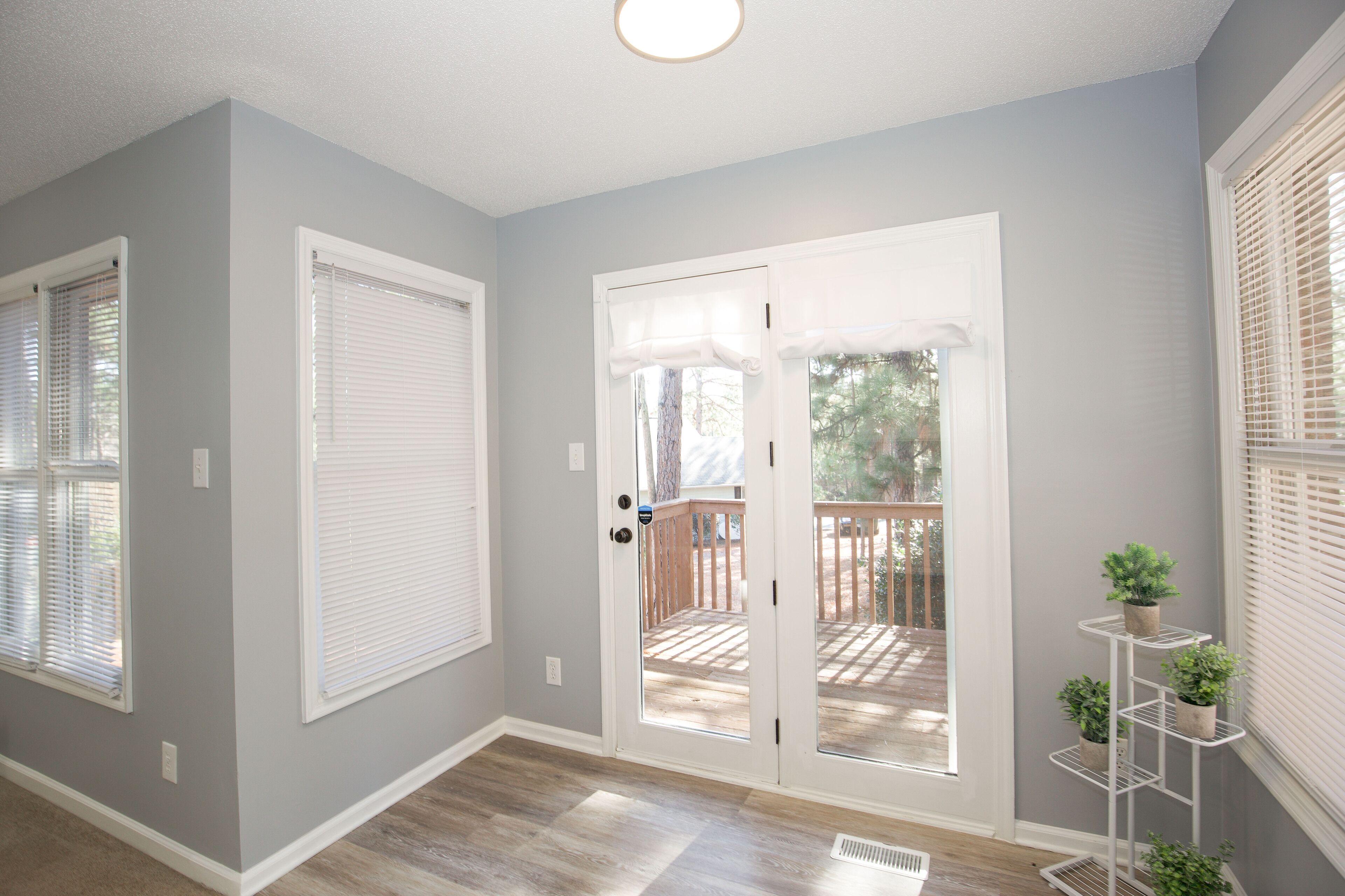 A hallway with a grey wall, white trim, and a wooden floor. There is a white door with glass panels leading to an outdoor deck.