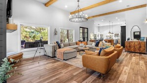 Un vaste espace de vie comprenant un grand canapé, un pouf et une table basse, un plancher en bois et un plafond haut avec des poutres apparentes.