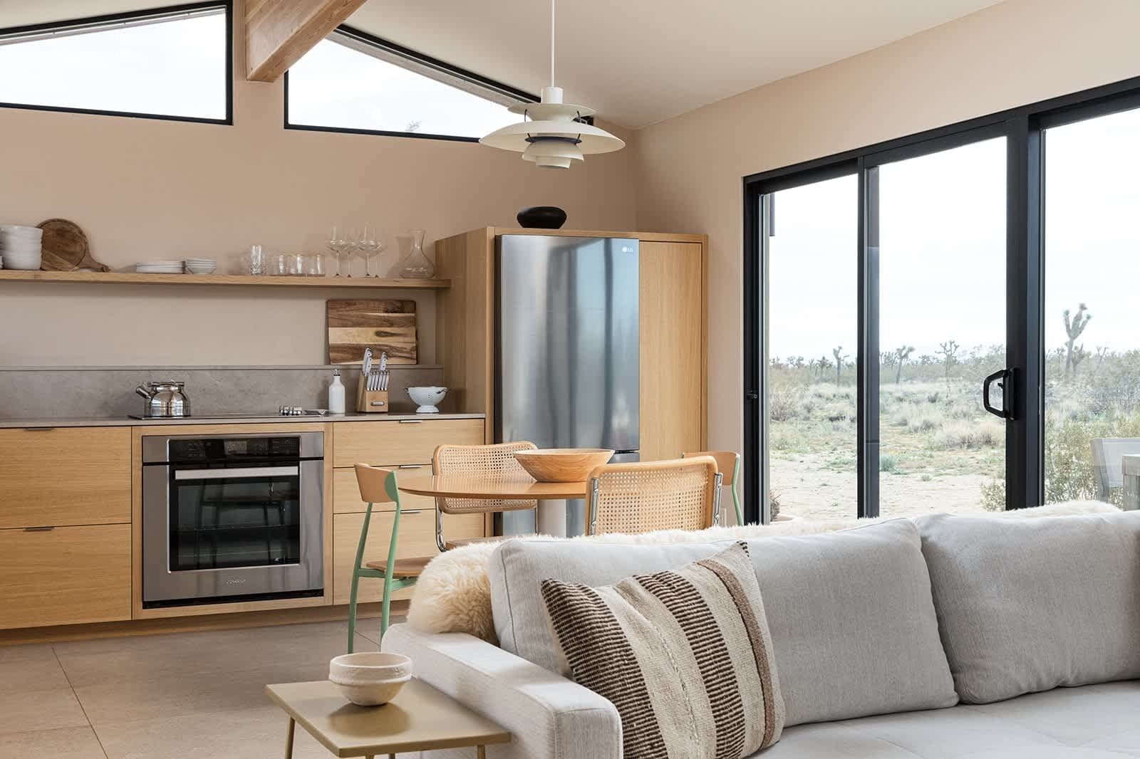 A modern kitchen with a built-in oven, a dining area with a table and chairs, and a large sliding glass door leading to an outdoor area.