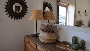 A wooden dresser with a mirror, two lamps, a woven basket with dried plants, and a tray with cacti and a small bowl. - CANYELLES PETITES - ROSAS 3mn plage Vue mer Tout confort GARAGE Terrasse 40m2 (Roses)