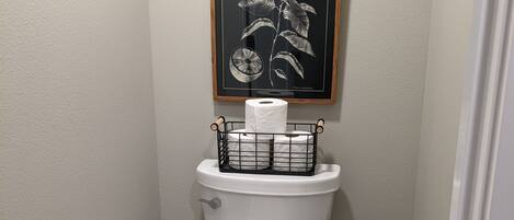 Een badkamer met een toilet, een ingelijste botanische afbeelding en een toiletrolhouder met een rol.