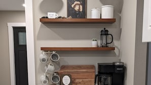 Een keuken met grijze kastjes, een koffiezetapparaat, mokken, en een bordje met de tekst 'Our Little Coffee Bar'.
