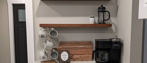 Una cocina con gabinetes grises, una cafetera, tazas y un letrero que dice 'Our Little Coffee Bar'.