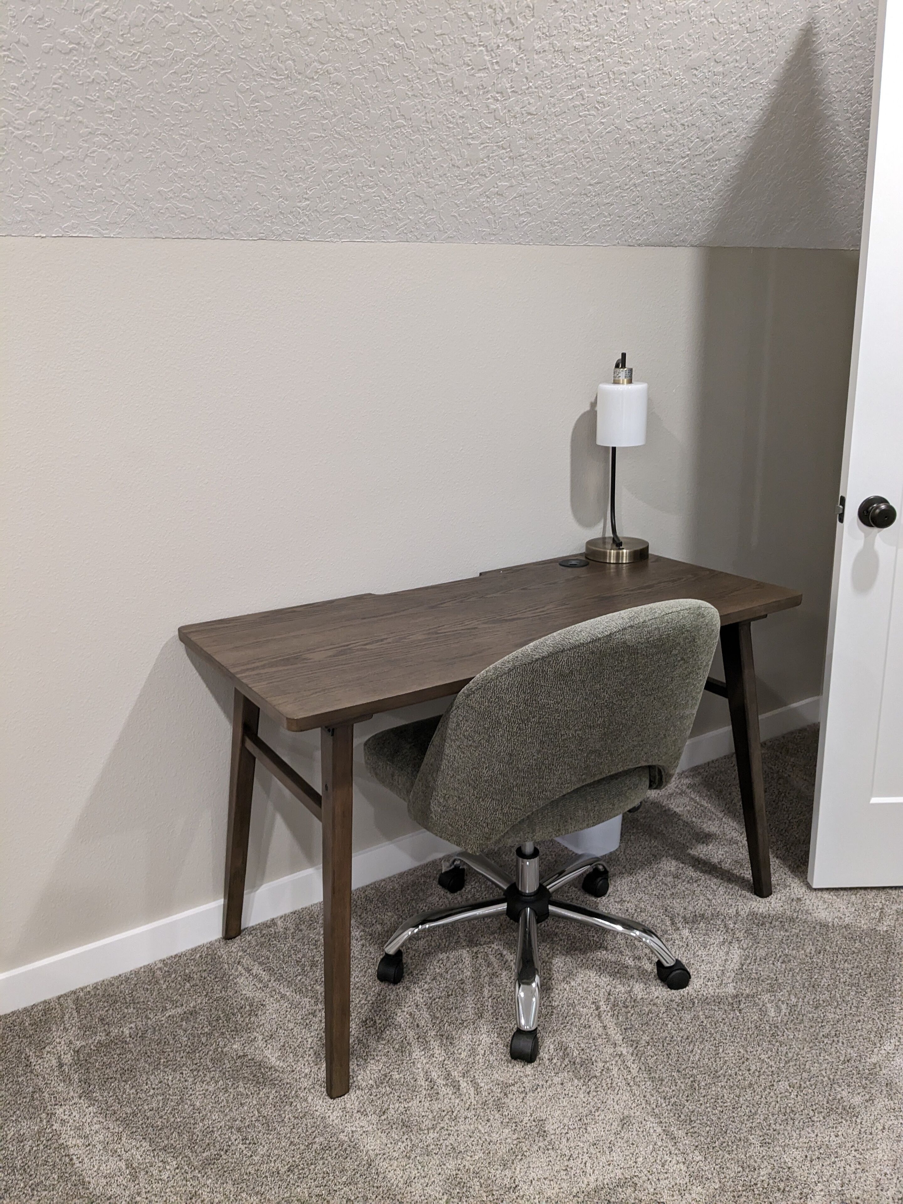 A small office space with a wooden desk, a grey office chair, and a white desk lamp.