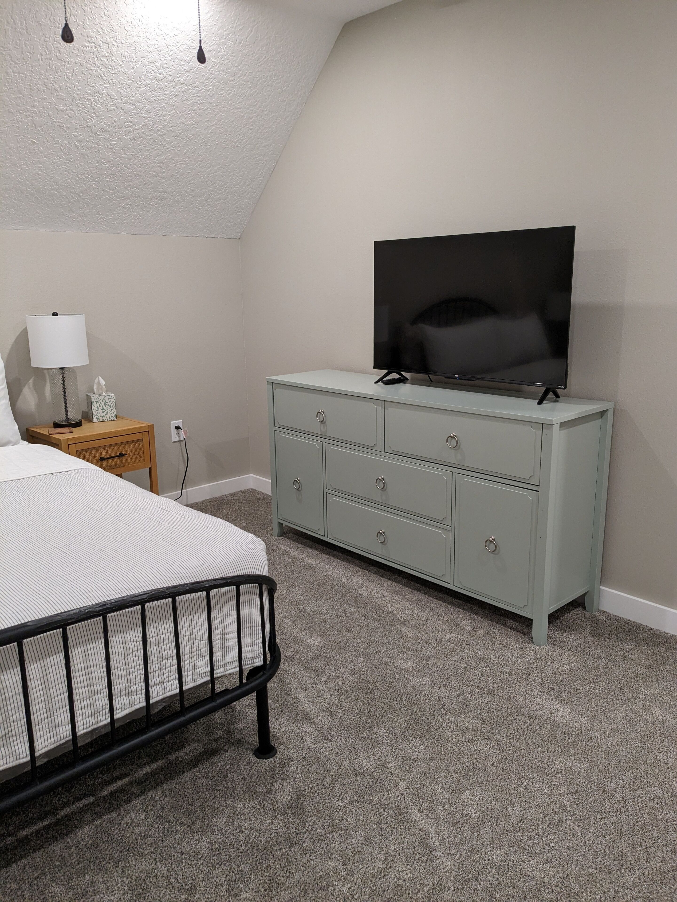 A bedroom with a bed, a dresser, a television, and a lamp.
