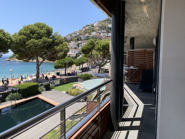 Un balcon avec vue sur une plage, une piscine et des bâtiments situés sur une colline.