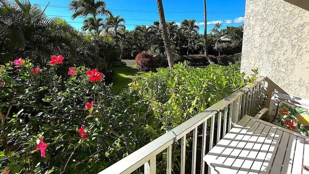 Een balkon met uitzicht op een tuin met palmboompjes en rode bloemen.