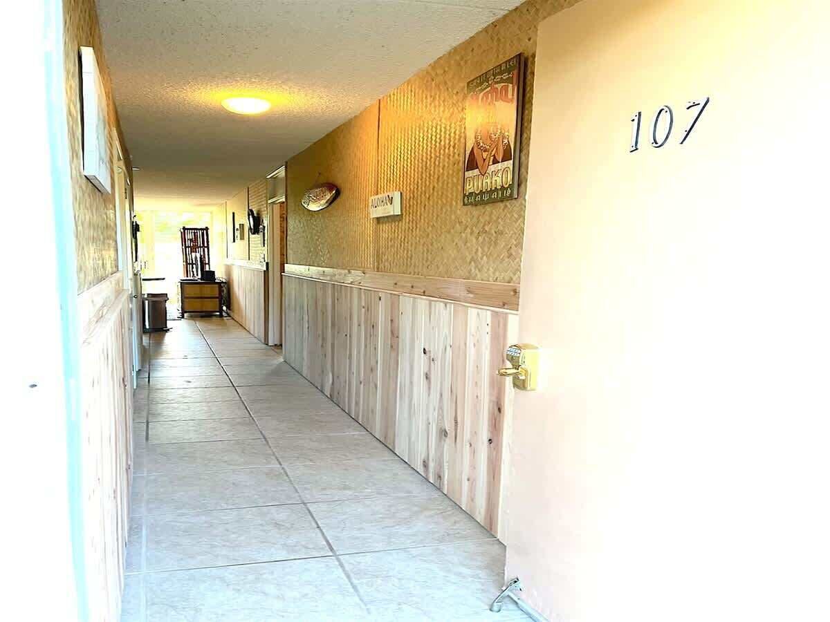 Un pasillo con paneles de madera, suelo de baldosas y una puerta con el número 107.