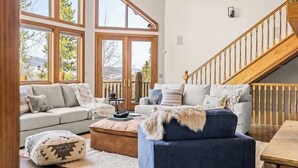 A spacious living room with large windows, a wooden staircase, and a cozy seating area with a sofa and ottoman. - Western Sky Ranch | 8 Bed | Pool Table + Deck (Breckenridge)
