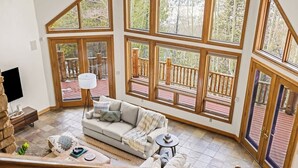 A spacious living area with a large window overlooking a wooden deck, a sofa, and a coffee table. - Western Sky Ranch | 8 Bed | Pool Table + Deck (Breckenridge)