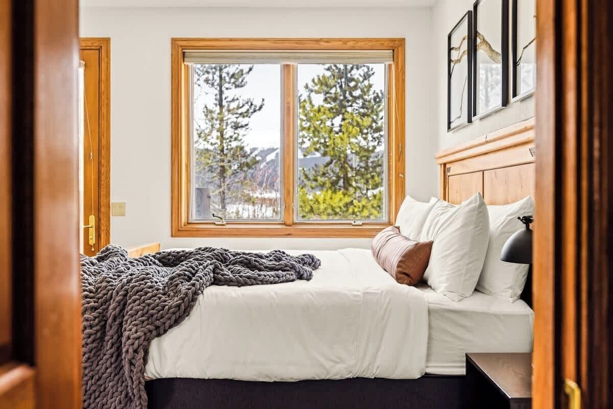 A bedroom with a large window, a bed with white bedding, and a wooden headboard.