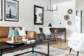 A modern living room with a brown leather sofa, a black coffee table, and a dining area with a wooden table and chairs. - Keystone Lake w/ MTN View | Pool+Hot Tub+Gym+Sauna (Dillon)