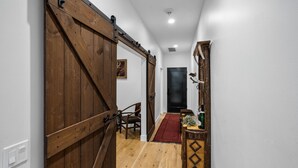 Un couloir avec une porte coulissante en bois, une moquette rouge et une décoration rustique comprenant une table en bois, une bouteille et quelques plantes.