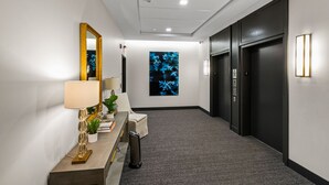 Un couloir avec un bureau, un miroir, une plante et une œuvre d’art accrochée au mur.