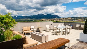 Une terrasse sur le toit, aménagée avec du mobilier d’extérieur, un foyer et offrant une vue sur les montagnes.