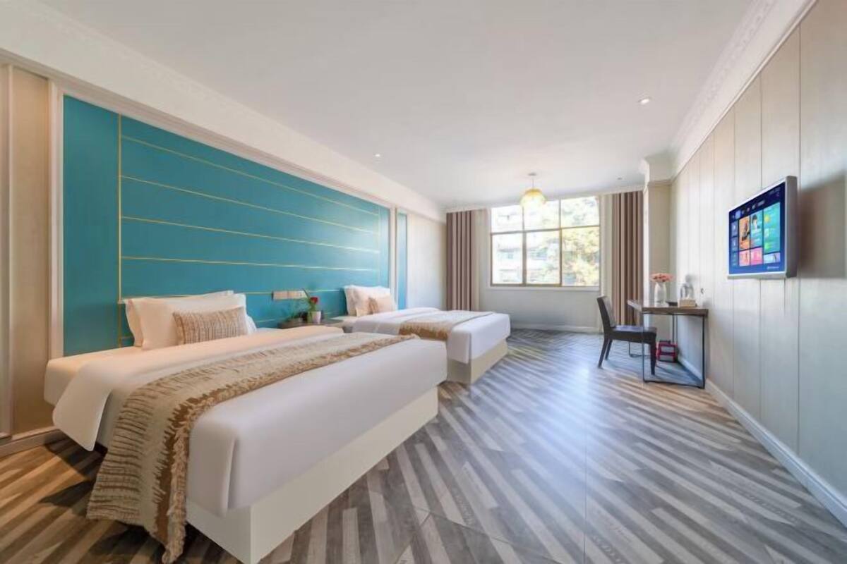A hotel room with two beds, a desk, a chair, and a TV on the wall.