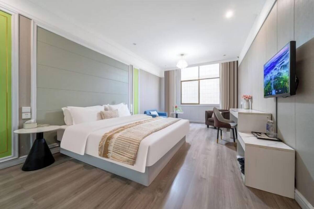 A modern hotel room with a bed, desk, chair, TV, and a window.