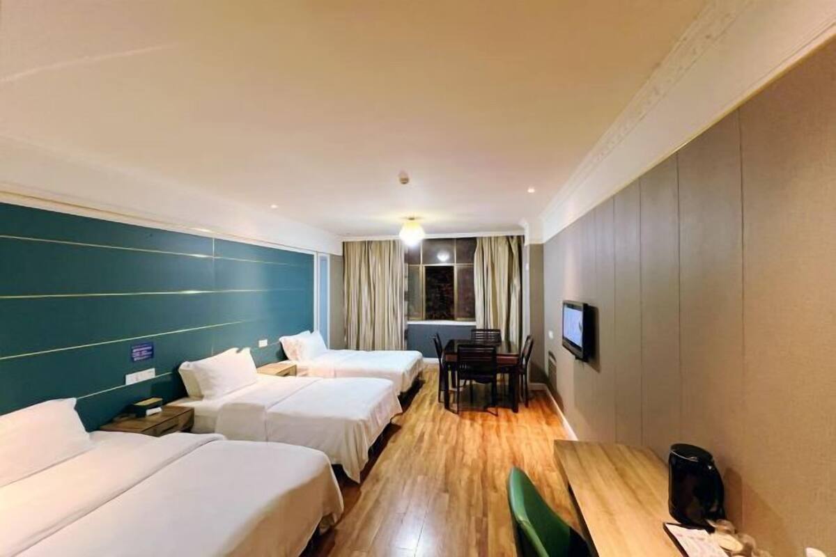 A hotel room with three single beds, a wooden dining table, a television, and a window with curtains.