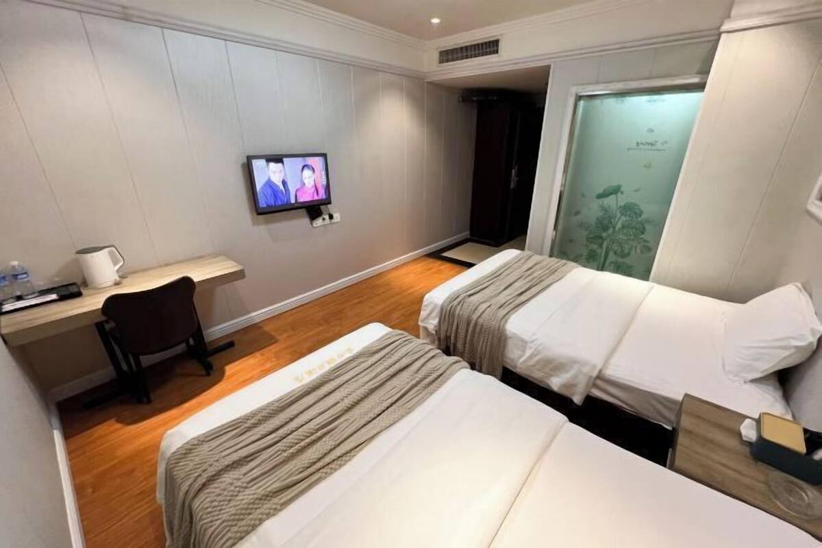 A hotel room with two beds, a desk, a chair, a television, and a wardrobe.
