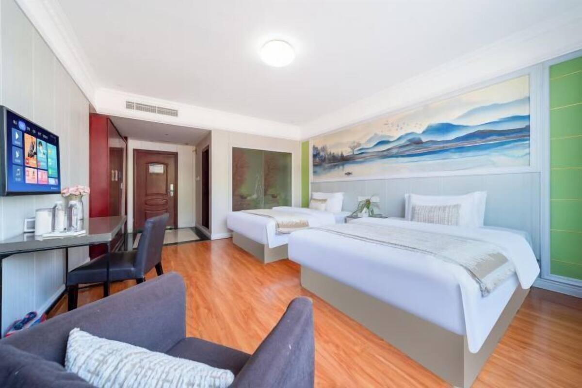 A hotel room with a bed, a desk, a chair, a TV, and a painting on the wall.