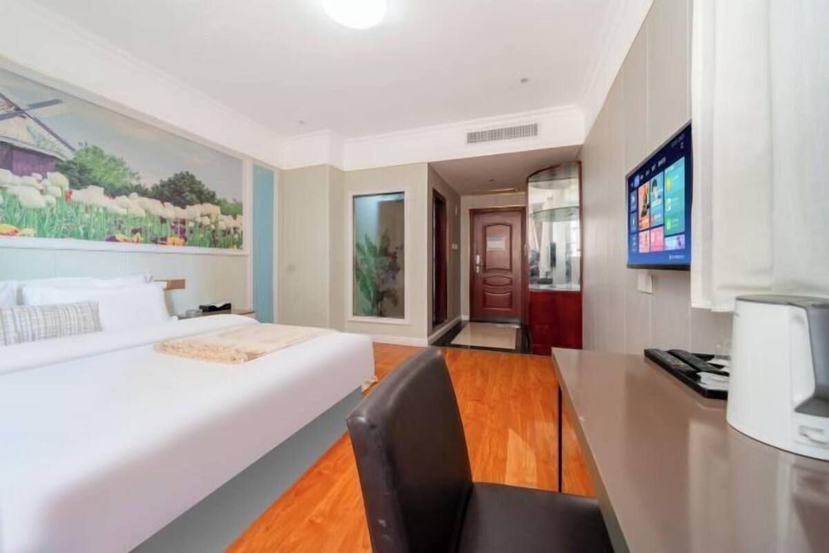 A hotel room with a bed, a desk, a chair, a painting on the wall, and a television.