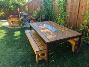 A wooden picnic table with benches in a backyard.