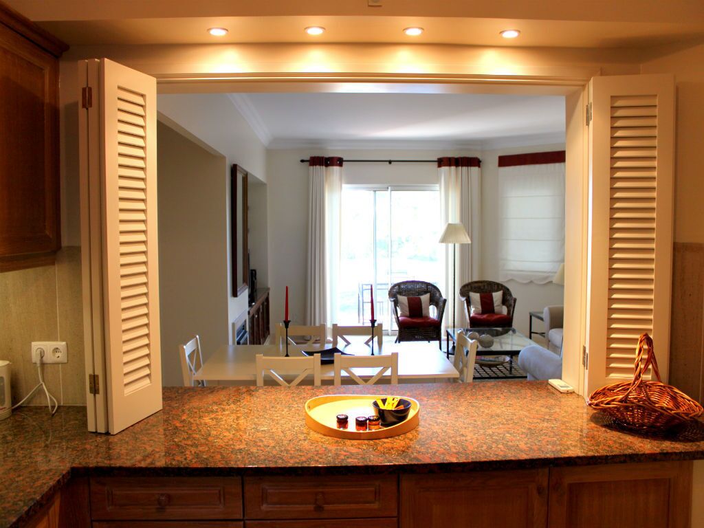 A kitchen with a granite countertop, a dining area with a table and chairs, and a view into a living room with a sofa and curtains.